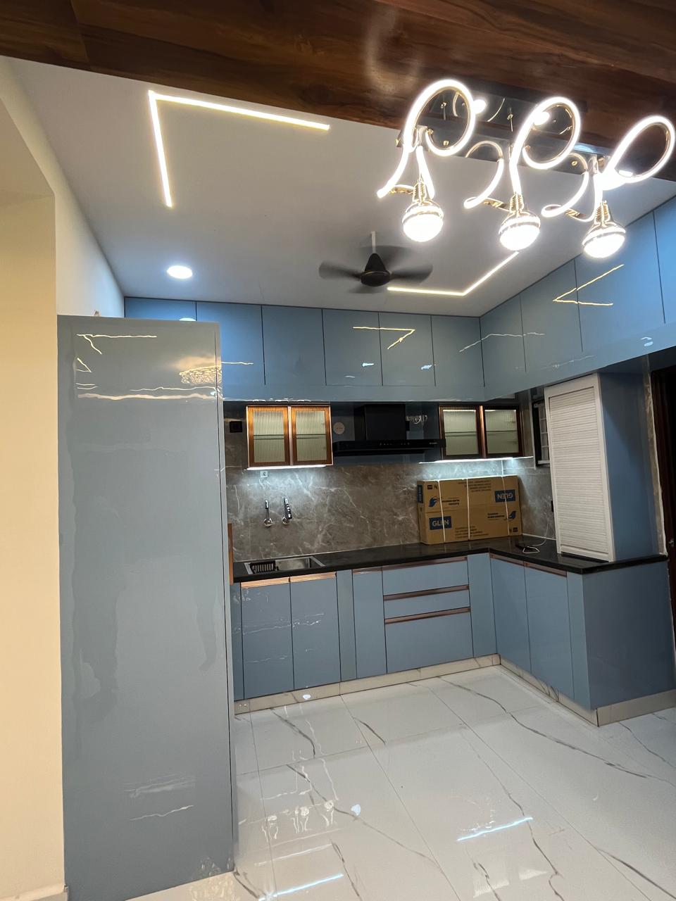 L-shaped glossy blue modular kitchen with designer lighting